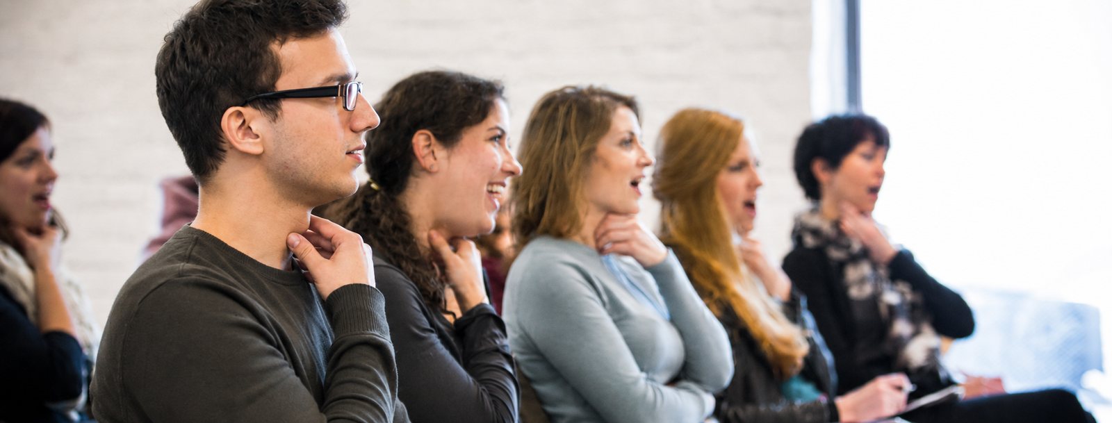 Teilnehmerinnen und Teilnehmer eines Vocalpower-Gesangsworkshops singen nebeneinander, die Hand am Kehlkopf, um die Stimmfunktion zu spüren